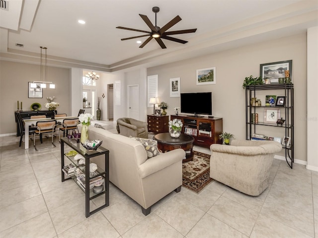 tiled living room with ceiling fan with notable chandelier and a tray ceiling