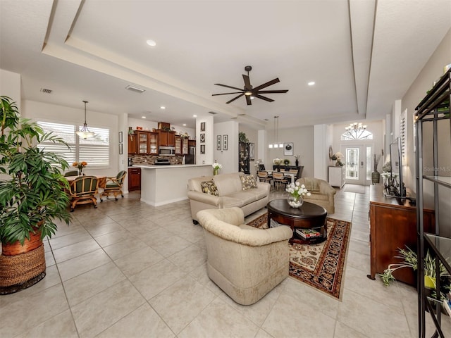 living room with ceiling fan with notable chandelier, french doors, a raised ceiling, and light tile patterned floors