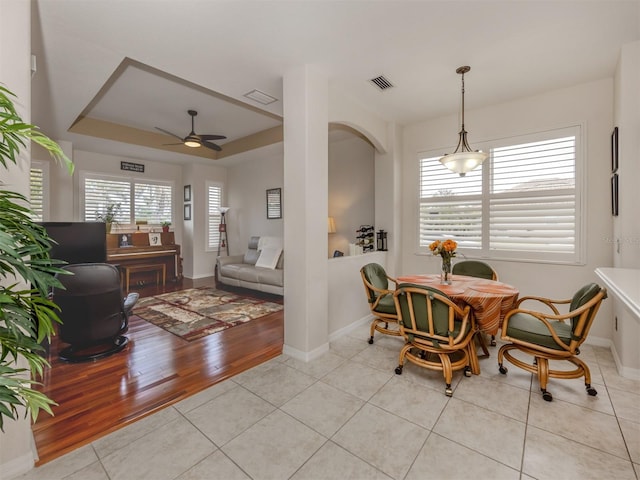 tiled dining space with a raised ceiling and ceiling fan