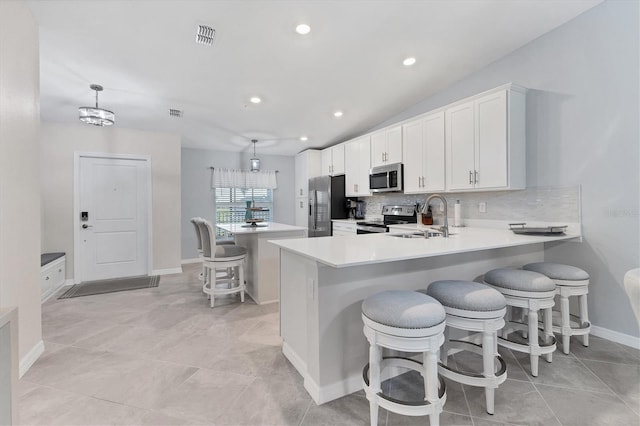 kitchen featuring kitchen peninsula, appliances with stainless steel finishes, a kitchen bar, sink, and pendant lighting