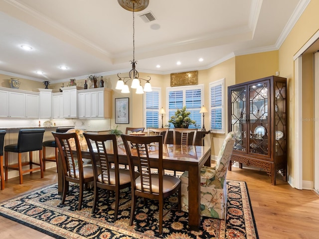 dining room with a chandelier, a raised ceiling, ornamental molding, and light hardwood / wood-style flooring