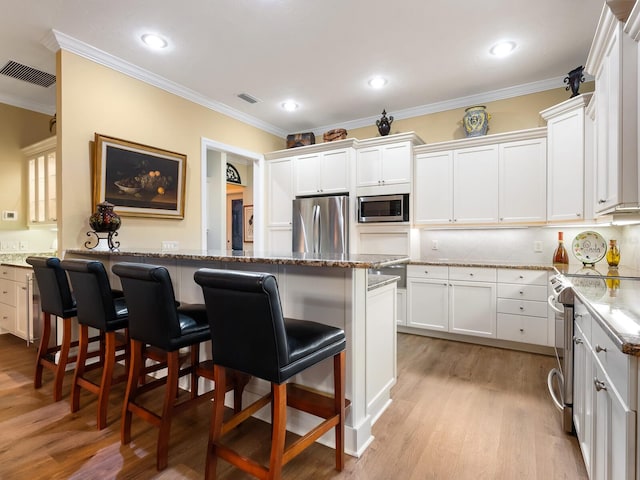 kitchen with stone counters, light wood-type flooring, appliances with stainless steel finishes, a kitchen bar, and white cabinetry