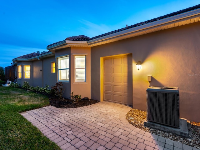 exterior entry at dusk with a garage and central air condition unit