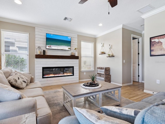 living room featuring ceiling fan, crown molding, hardwood / wood-style floors, a textured ceiling, and a fireplace