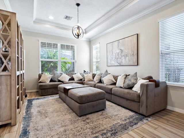 living room featuring an inviting chandelier, a raised ceiling, ornamental molding, a textured ceiling, and light hardwood / wood-style floors