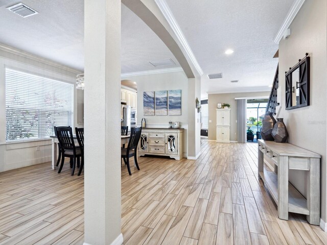 interior space with light hardwood / wood-style flooring, a chandelier, a textured ceiling, and ornamental molding