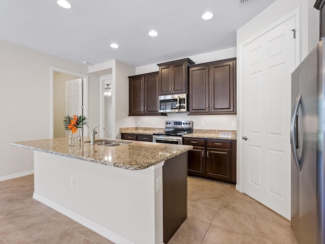 kitchen featuring light stone countertops, stainless steel appliances, sink, light tile patterned floors, and a center island with sink