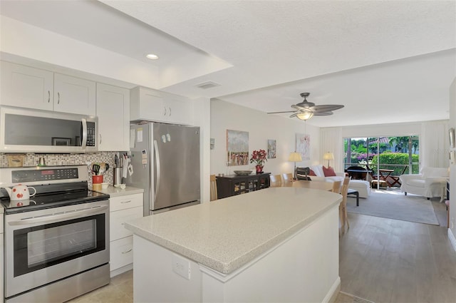 kitchen featuring backsplash, white cabinets, ceiling fan, a kitchen island, and stainless steel appliances