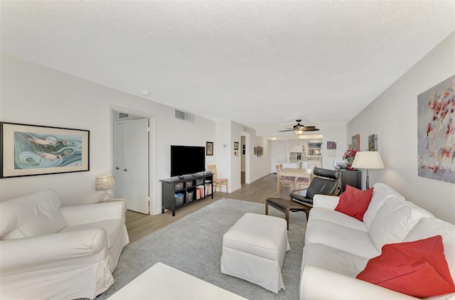 living room with ceiling fan, a textured ceiling, and light hardwood / wood-style flooring