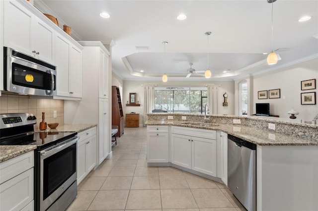 kitchen with a raised ceiling, white cabinetry, stainless steel appliances, and decorative light fixtures