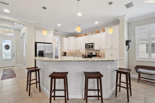 kitchen with pendant lighting, stainless steel appliances, white cabinetry, and a center island with sink