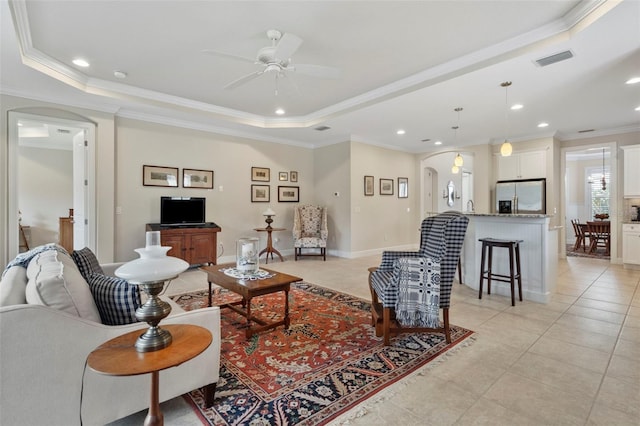 living room featuring a tray ceiling, ceiling fan, light tile patterned flooring, and ornamental molding