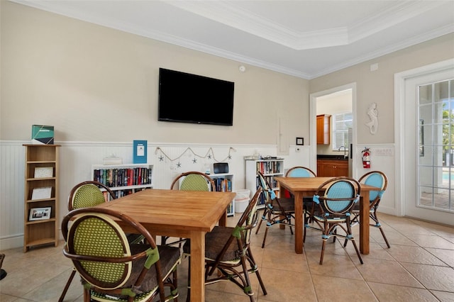 tiled dining space with sink, a raised ceiling, and crown molding