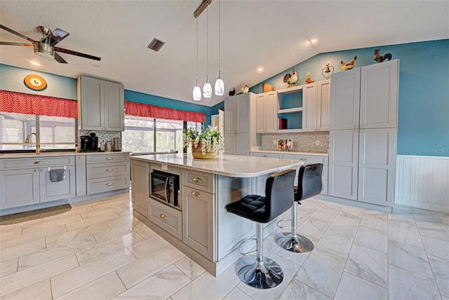 kitchen featuring gray cabinetry, black microwave, a textured ceiling, vaulted ceiling, and a kitchen island