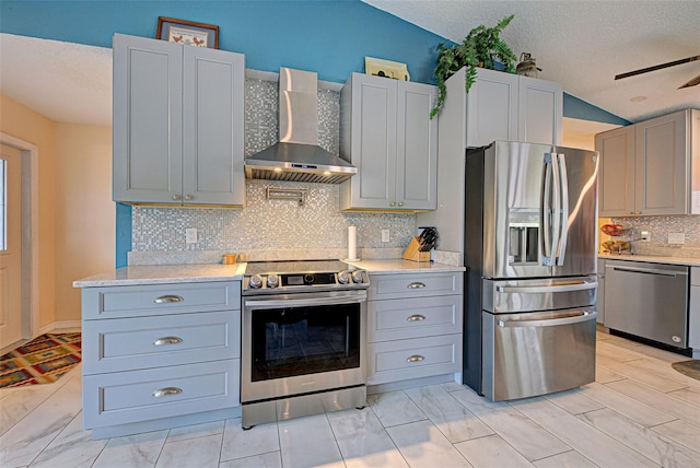 kitchen featuring vaulted ceiling, wall chimney exhaust hood, ceiling fan, a textured ceiling, and appliances with stainless steel finishes