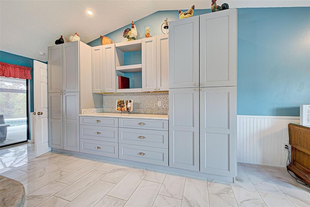 kitchen featuring a textured ceiling, gray cabinets, decorative backsplash, and lofted ceiling