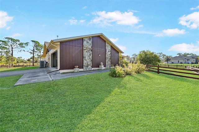 rear view of house with a lawn, central AC unit, fence, stone siding, and driveway