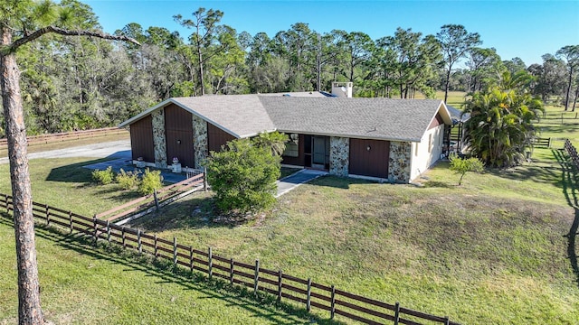 view of front facade with stone siding, fence, a front lawn, and roof with shingles