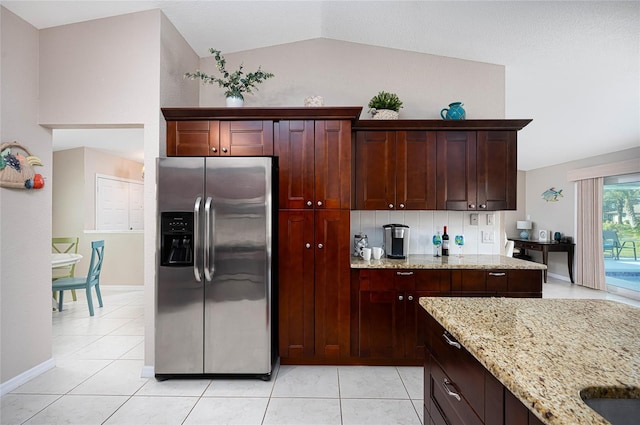 kitchen with light stone countertops, light tile patterned floors, vaulted ceiling, and stainless steel fridge