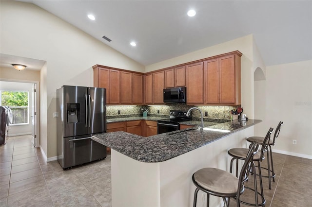 kitchen with kitchen peninsula, light tile patterned floors, a kitchen bar, black appliances, and lofted ceiling