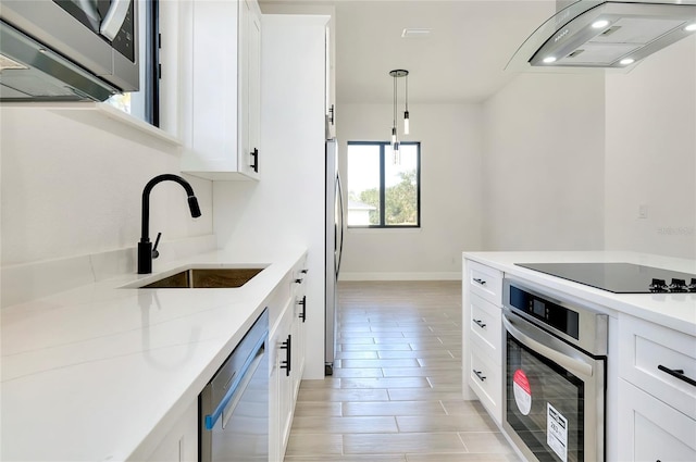 kitchen with hanging light fixtures, sink, range hood, white cabinetry, and stainless steel appliances