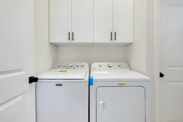 clothes washing area with washing machine and clothes dryer and cabinets