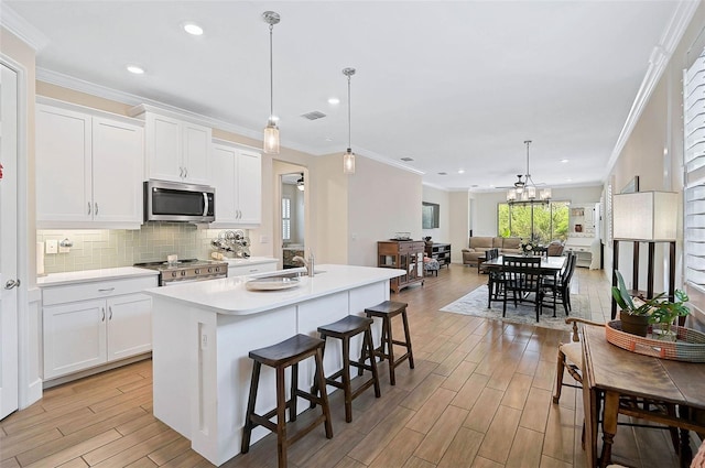 kitchen featuring white cabinets, an island with sink, hanging light fixtures, and appliances with stainless steel finishes