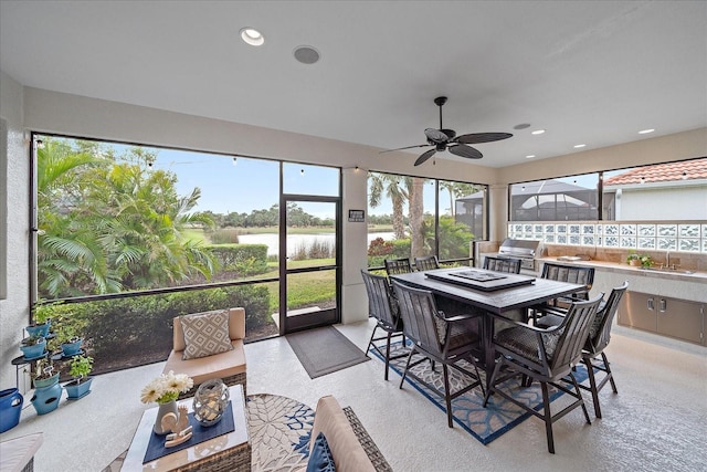 sunroom / solarium featuring plenty of natural light, a ceiling fan, a water view, and a sink