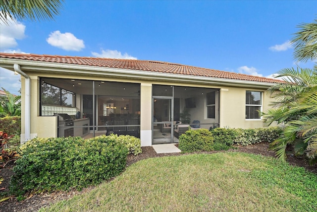 back of property with a tile roof, a lawn, a sunroom, and stucco siding