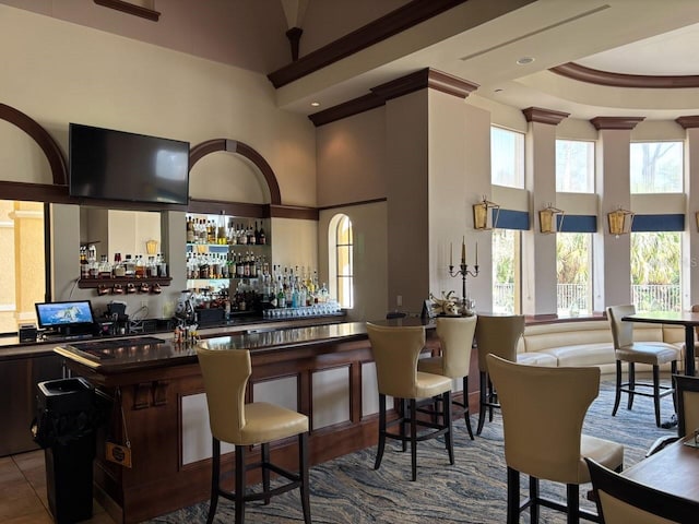 bar with a high ceiling, tile patterned floors, and plenty of natural light