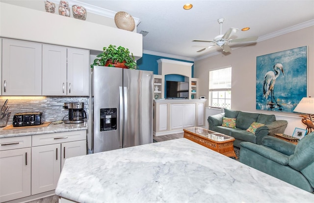 kitchen with stainless steel fridge, backsplash, light stone counters, ceiling fan, and crown molding