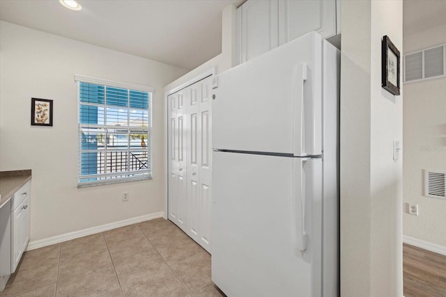 kitchen featuring white cabinets, white refrigerator, and light tile patterned flooring