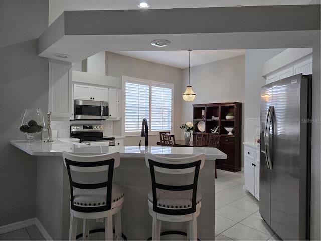 kitchen featuring white cabinets, a kitchen breakfast bar, appliances with stainless steel finishes, light tile patterned flooring, and kitchen peninsula