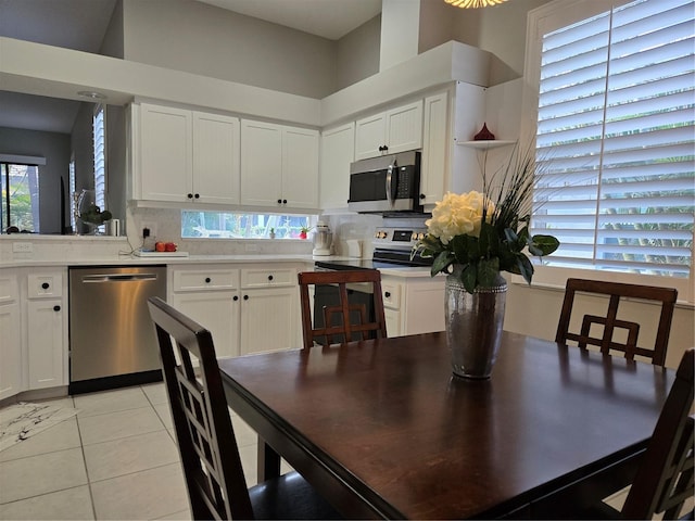 kitchen with white cabinets, appliances with stainless steel finishes, a high ceiling, and light tile patterned flooring