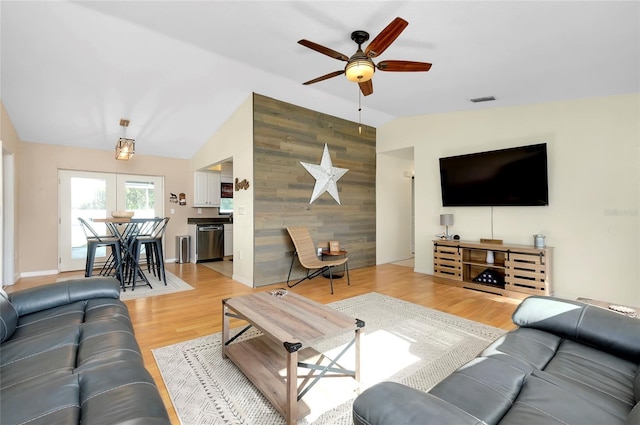 living room featuring wood walls, light hardwood / wood-style flooring, ceiling fan, and lofted ceiling