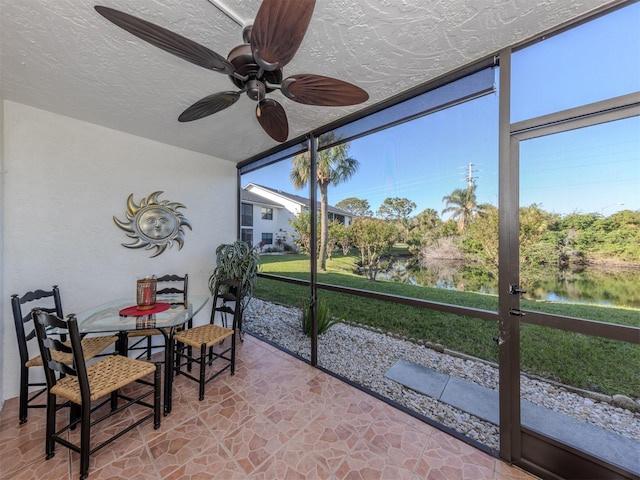 sunroom with ceiling fan and a water view