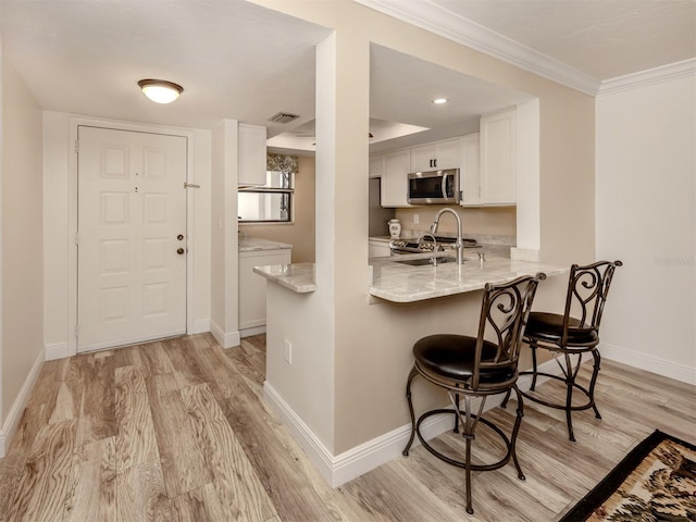 kitchen with kitchen peninsula, appliances with stainless steel finishes, light hardwood / wood-style floors, white cabinets, and ornamental molding