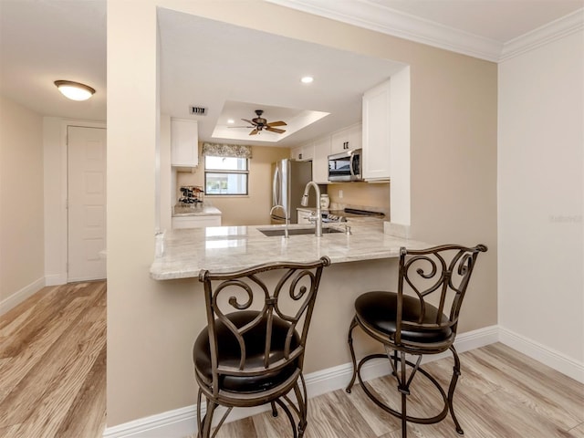 kitchen with kitchen peninsula, a tray ceiling, a kitchen bar, white cabinetry, and stainless steel appliances