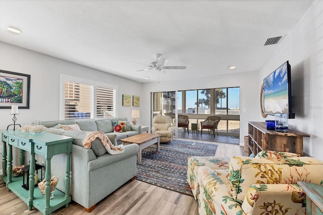 living room featuring ceiling fan, a textured ceiling, and light wood-type flooring