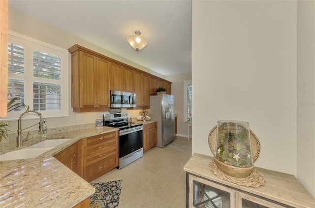 kitchen with light stone countertops, stainless steel appliances, a sink, and brown cabinetry