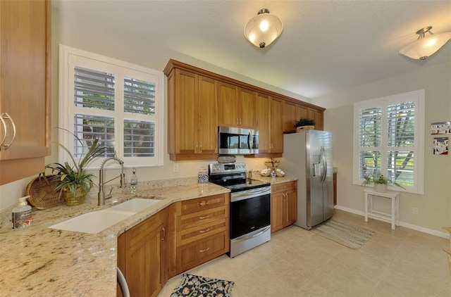 kitchen featuring brown cabinets, light tile patterned floors, appliances with stainless steel finishes, a sink, and light stone countertops