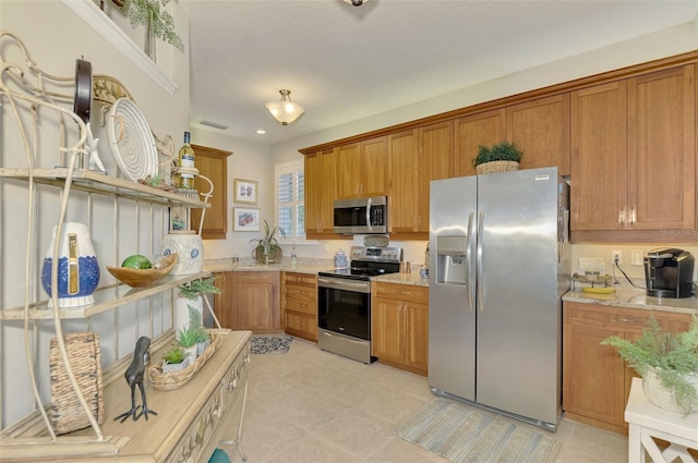 kitchen featuring light tile patterned floors, light stone counters, stainless steel appliances, visible vents, and brown cabinets