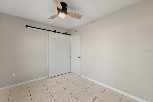 tiled empty room with ceiling fan and a barn door