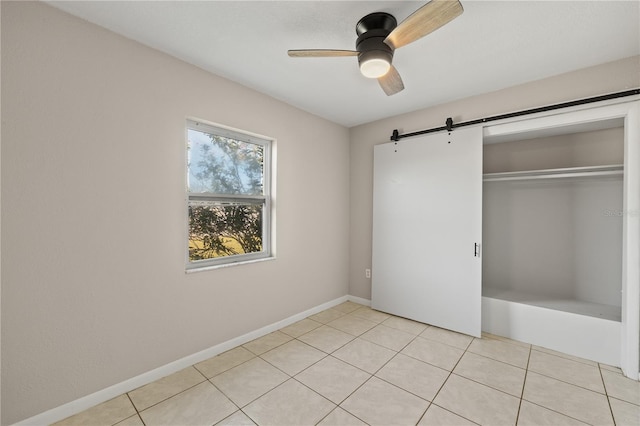 unfurnished bedroom with light tile patterned floors, a barn door, a closet, and ceiling fan