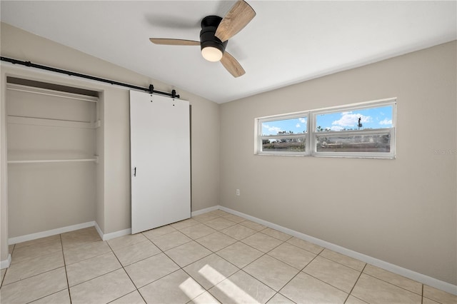 unfurnished bedroom featuring vaulted ceiling, ceiling fan, a barn door, light tile patterned floors, and a closet