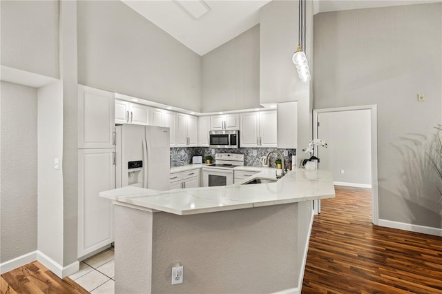 kitchen featuring sink, kitchen peninsula, a towering ceiling, white appliances, and white cabinets