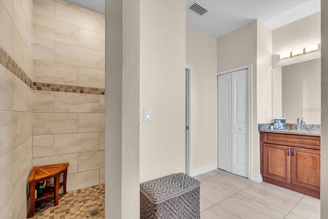 bathroom featuring tiled shower, vanity, and tile patterned flooring