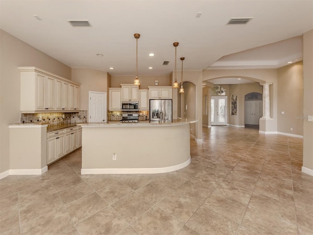 kitchen with pendant lighting, appliances with stainless steel finishes, decorative columns, a center island with sink, and decorative backsplash