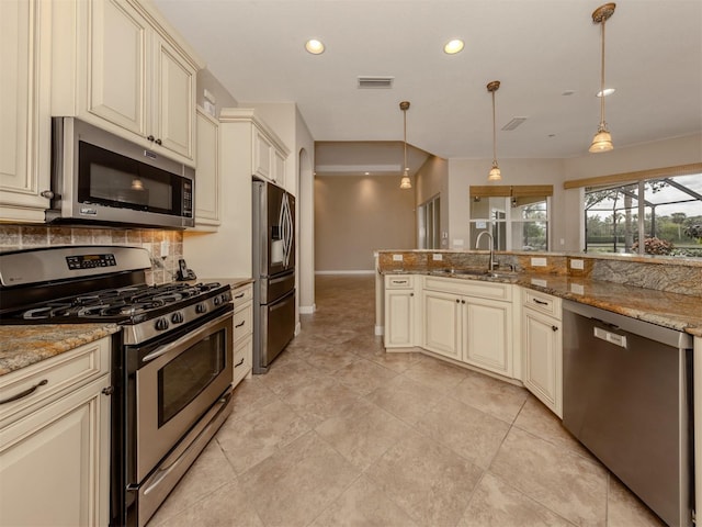 kitchen with stainless steel appliances, hanging light fixtures, light stone counters, and cream cabinetry