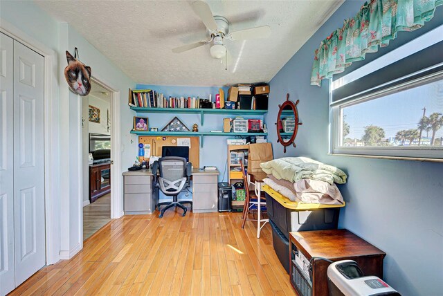 home office featuring ceiling fan, light hardwood / wood-style floors, and a textured ceiling